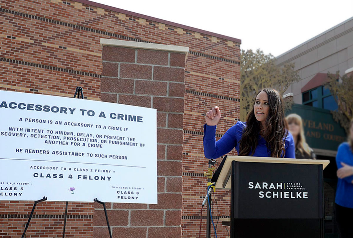 Sarah Schielke featured behind a podium in a press conference fearlessly defending her clients who were harassed by Loveland Police - Photo Credit Jenny Sparks of the Loveland Reporter-Herald